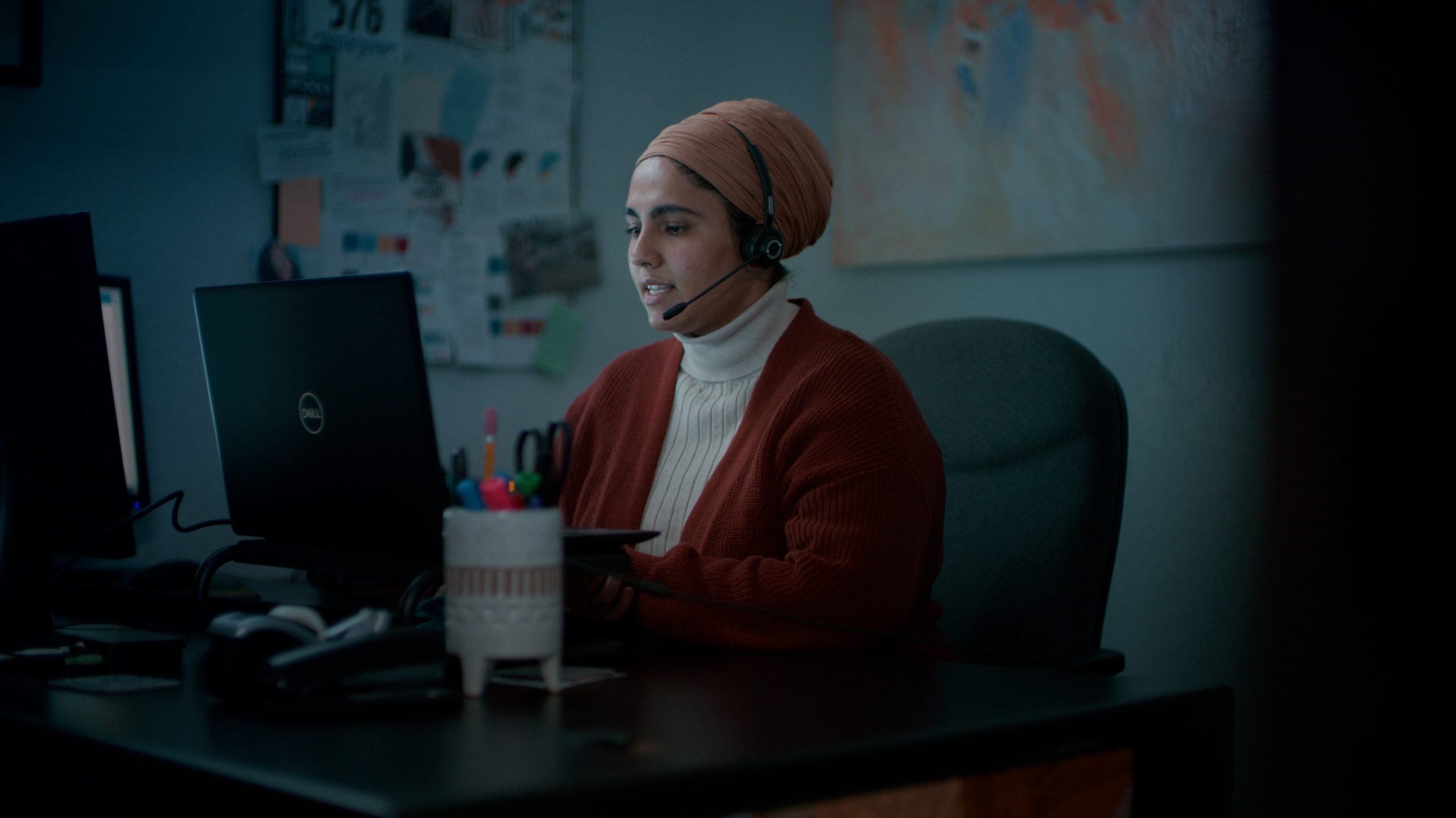 A picture of a woman with a telephone a headset sitting in front of a computer screen answering a 211 Helpline call
