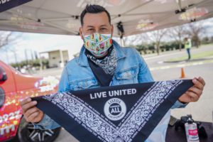 One of our partners wearing a mask and a denim jacket holding up a Live United Listos bandana