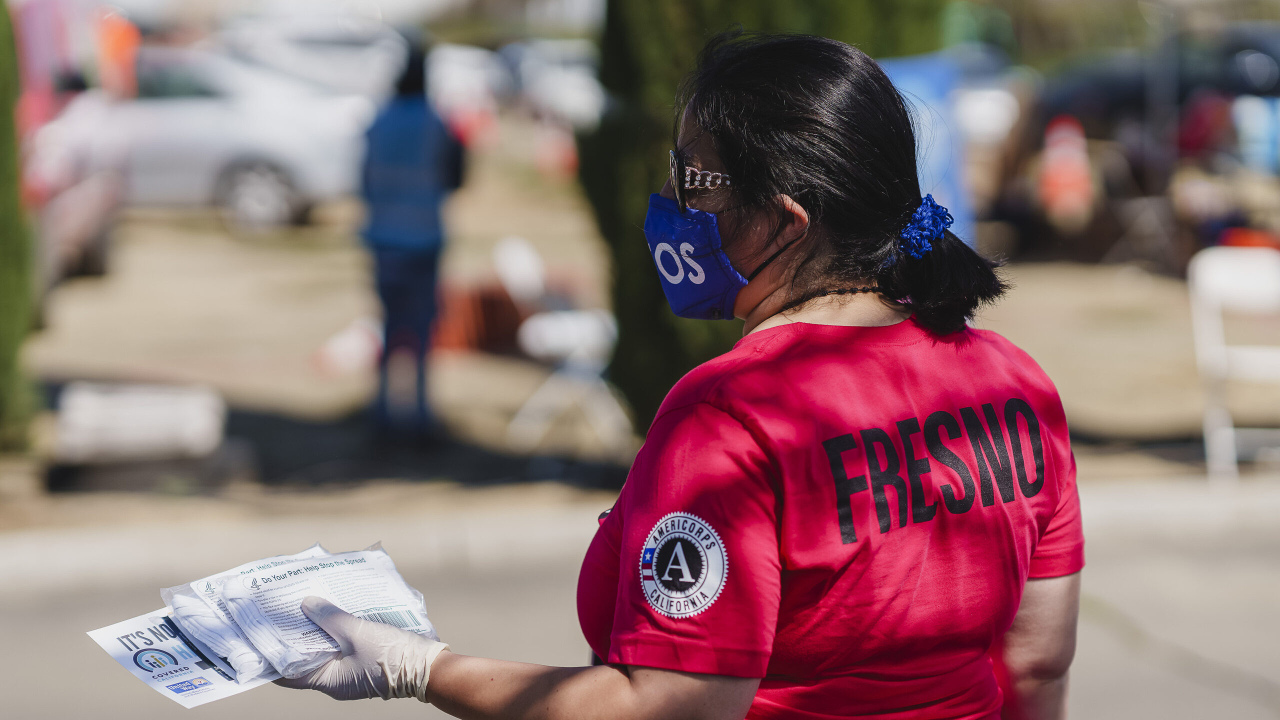 An Americorps volunteer with a shirt that has the word Fresno on the back hands out United Way Fresno and Madera Counties literature at an outdoor event