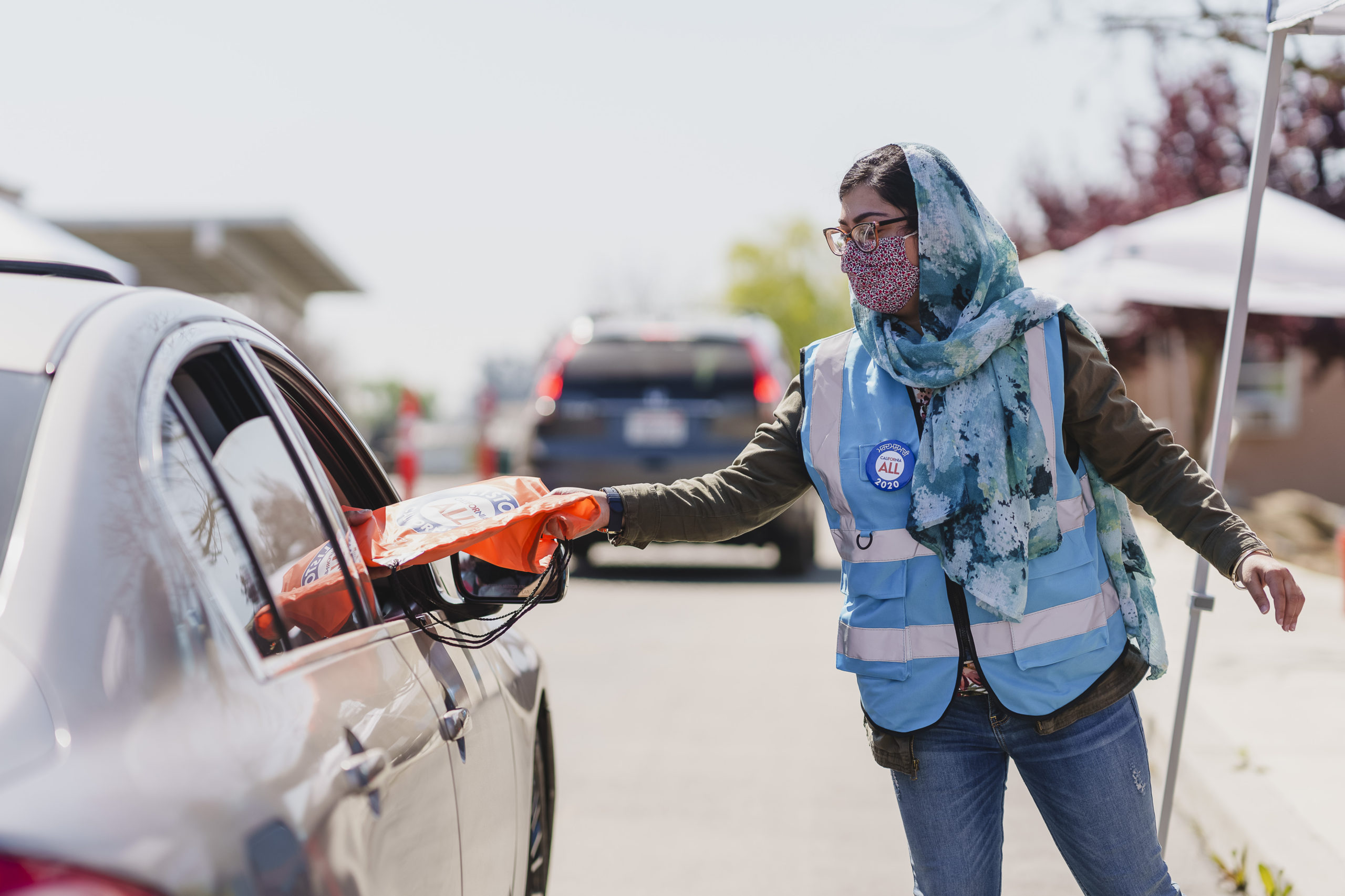 A volunteer gives a support package to someone in a car at an outdoor event.
