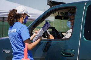 A volunteer hands out information packets to someone in a grey truck.
